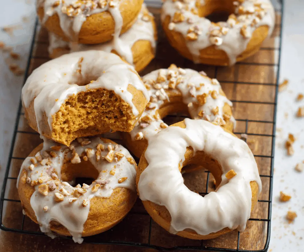 Golden baked pumpkin donuts topped with cinnamon glaze and sprinkles, served on a white plate for a delicious fall treat.