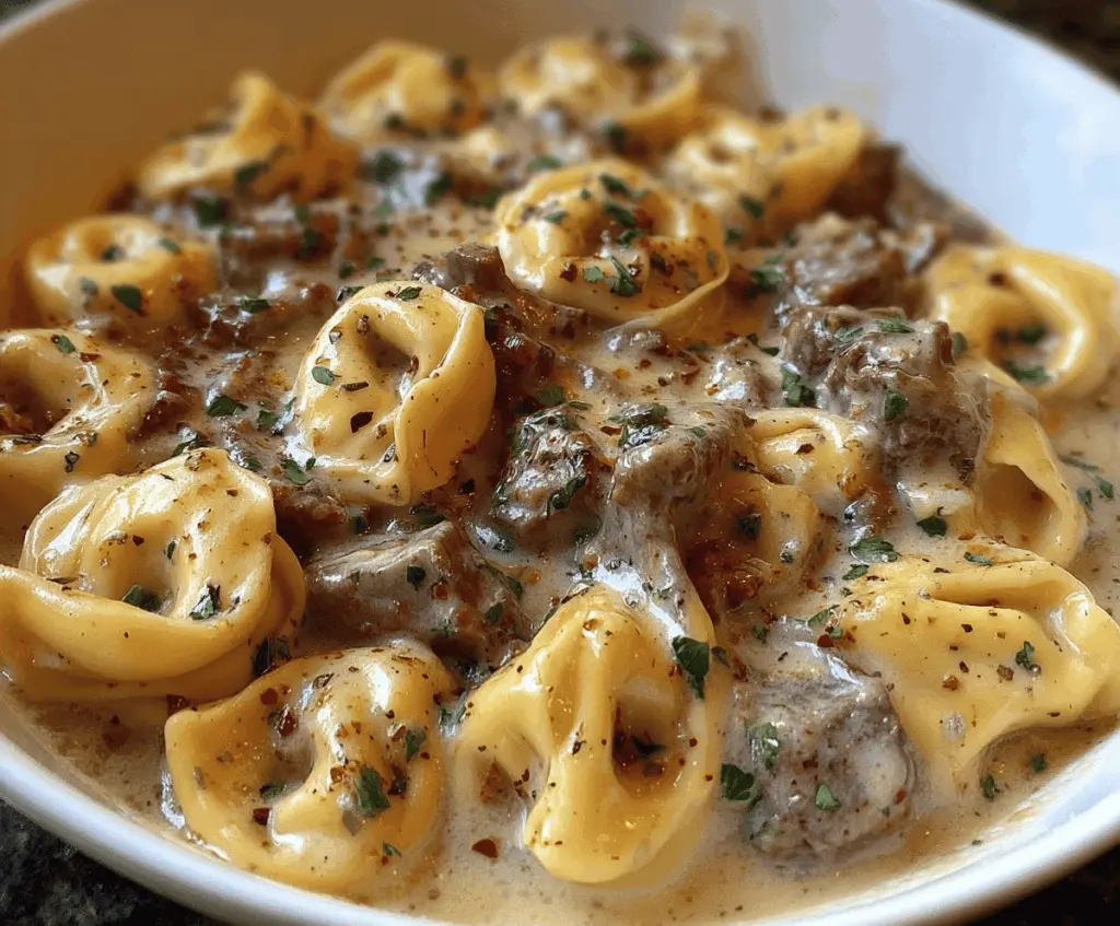 Creamy cheesesteak tortellini with melted provolone cheese in a flavorful sauce served on a plate