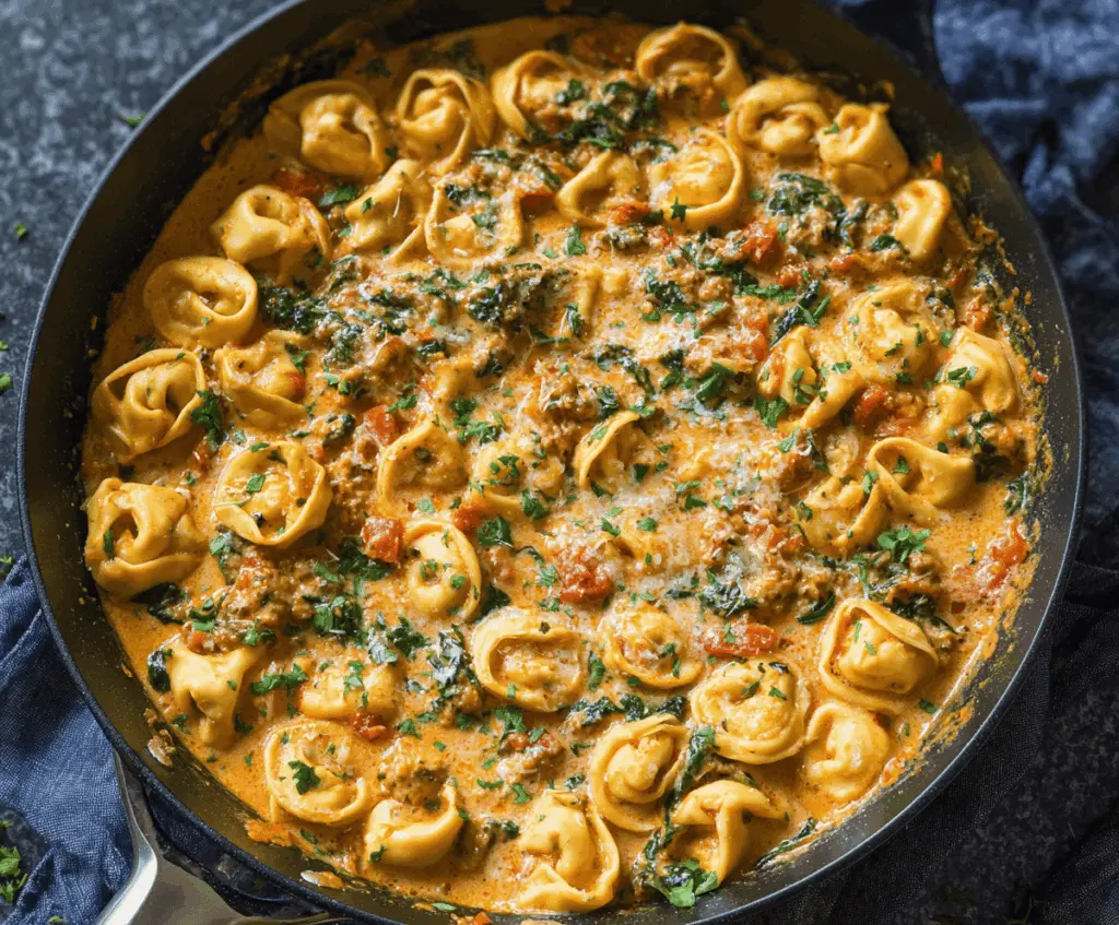 Creamy spinach and tomato tortellini dish garnished with fresh herbs on a white plate, featuring vibrant red tomatoes, green spinach, and tender tortellini in a creamy sauce.
