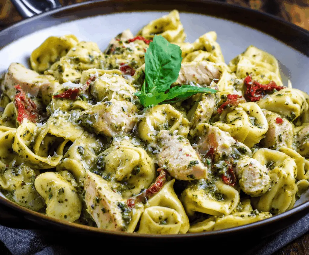 Creamy pesto chicken tortellini pasta dish garnished with fresh basil and grated Parmesan cheese, served on a white plate.