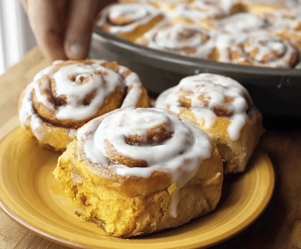 Delicious homemade pumpkin cinnamon rolls topped with creamy icing and sprinkled with cinnamon, perfect for fall breakfast or dessert.