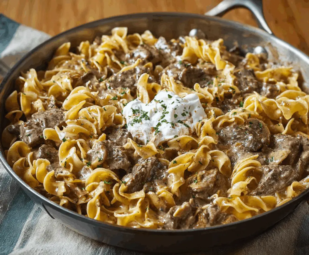 Creamy beef stroganoff served over noodles, garnished with fresh herbs on a white plate.