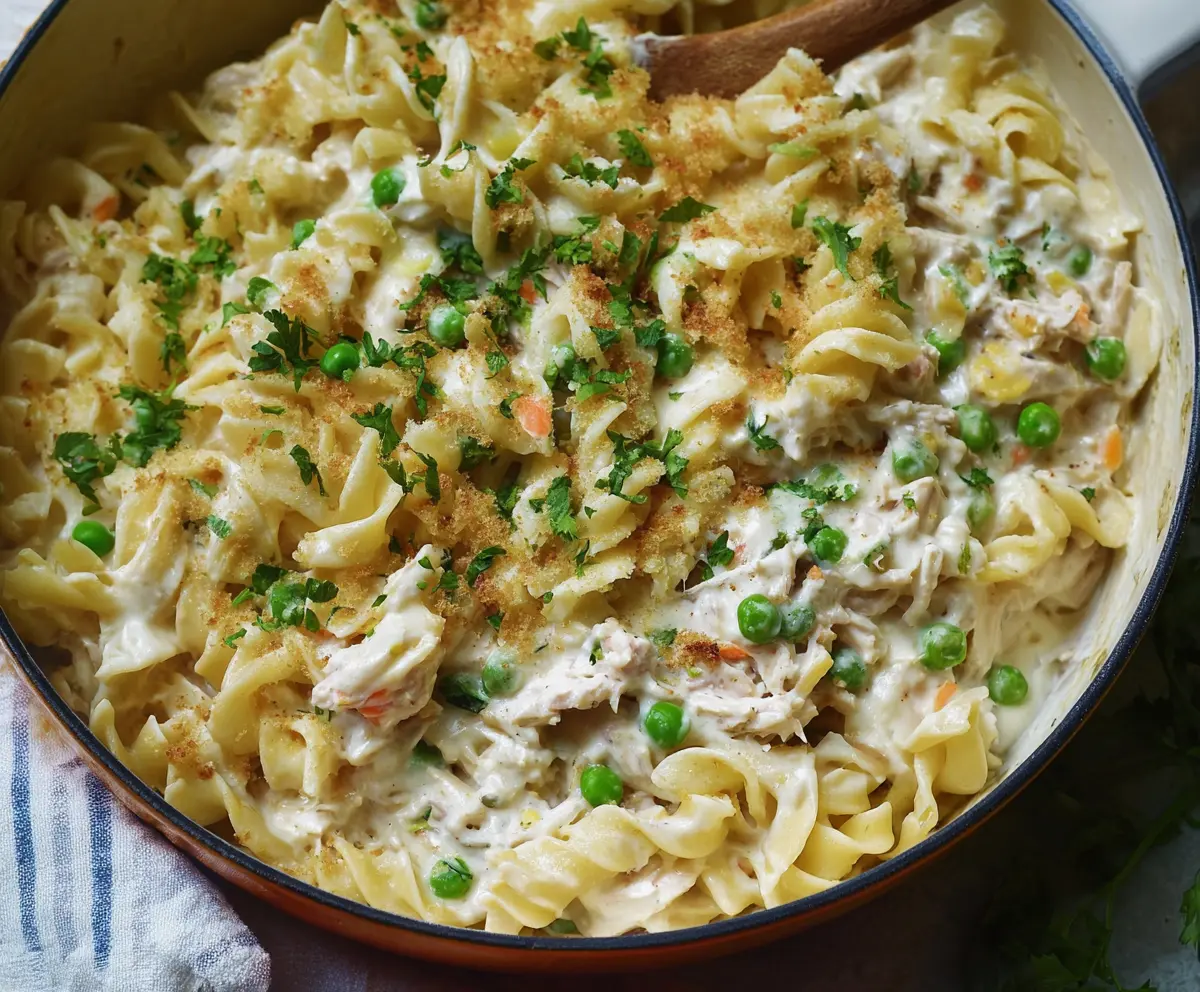 Creamy Tuna Noodle Casserole served in a baking dish with garnished herbs, showcasing a comforting and cheesy seafood pasta dish.